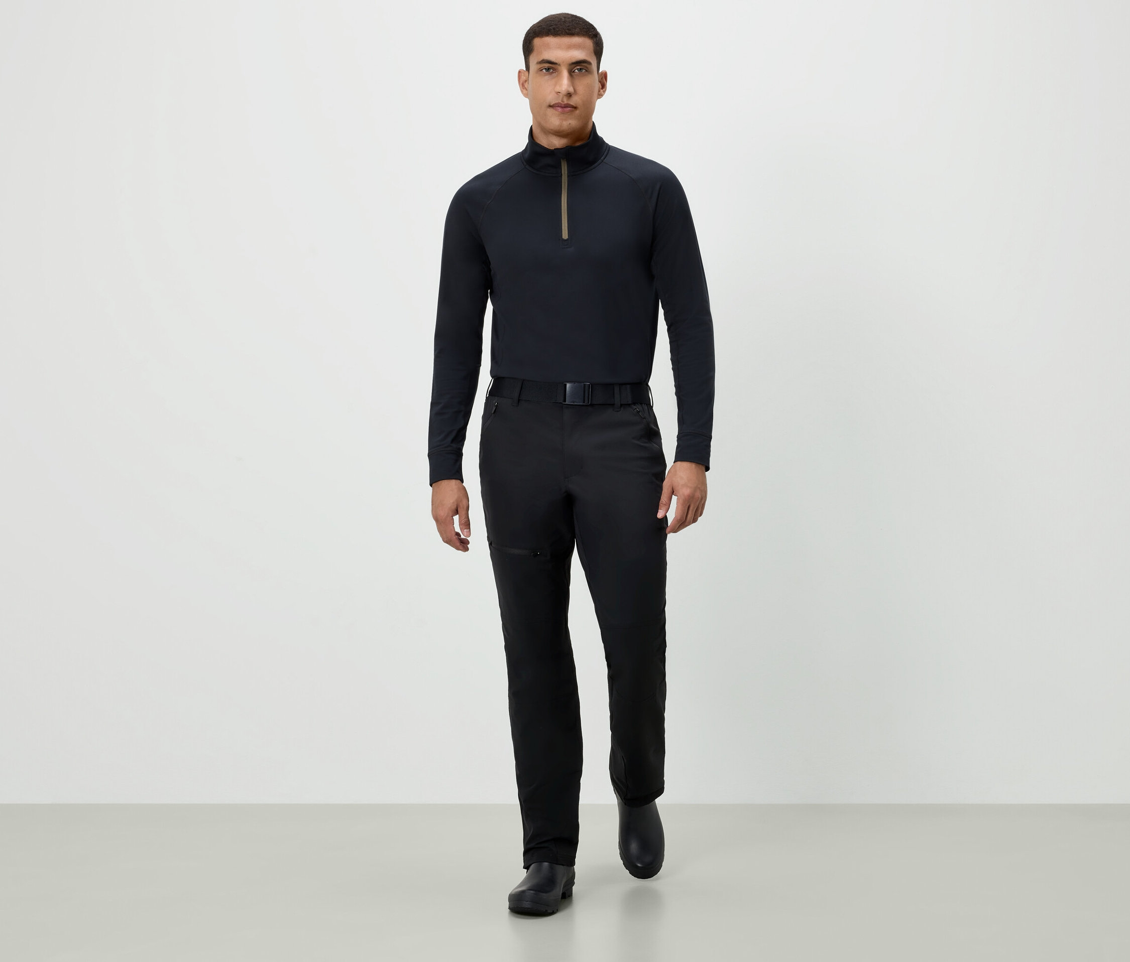 Un homme marche vers l'avant, portant un t-shirt noir à manches longues, un pantalon noir et des chaussures noires.