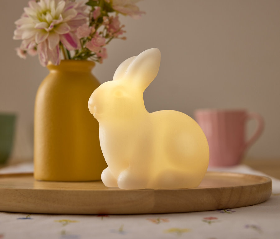 Vase jaune avec des fleurs, lumière de lapin jaune et tasses sur un plateau en bois.