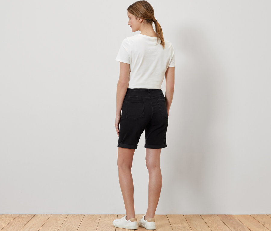 Femme vue de dos portant un bermuda en jean coupe « Lea » en denim noir, un t-shirt blanc et des baskets.