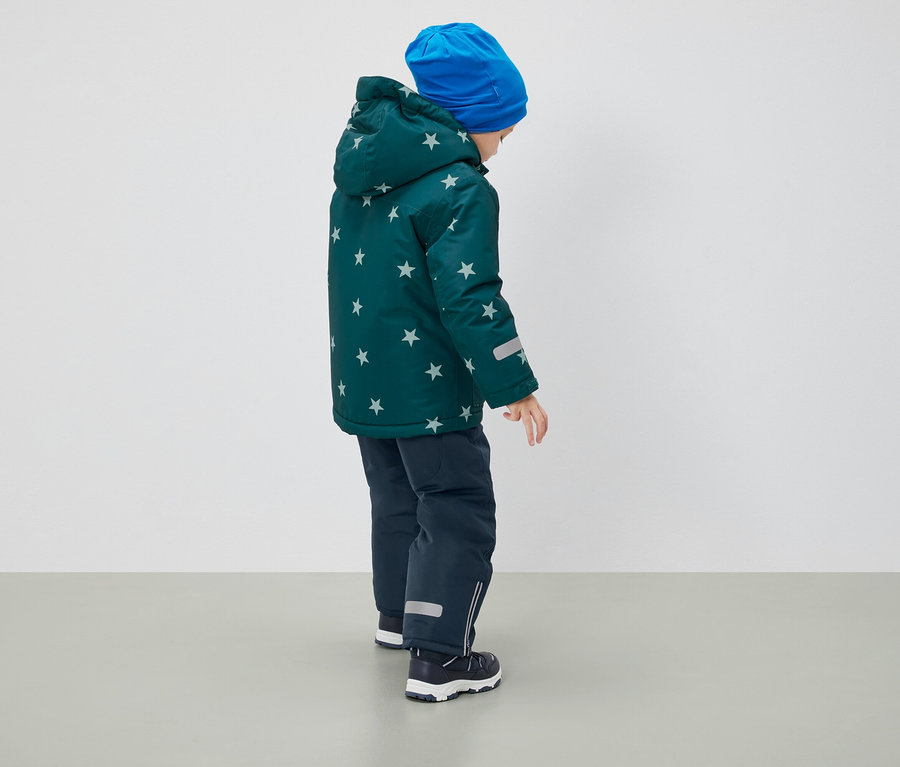 Un garçon, vu de dos, porte un manteau d'hiver à motif étoilé, un bonnet bleu et un pantalon bleu marine.