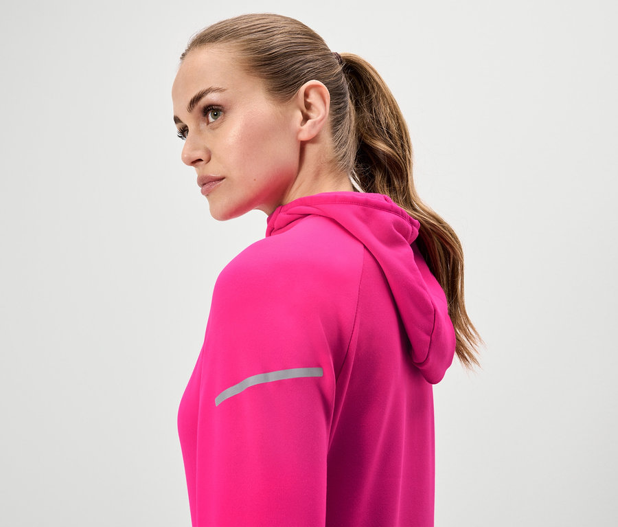 Femme aux cheveux bruns attachés en queue de cheval portant un sweat à capuche rose.