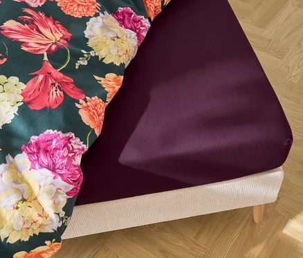 Lit avec drap-housse violet et linge de lit à fleurs.