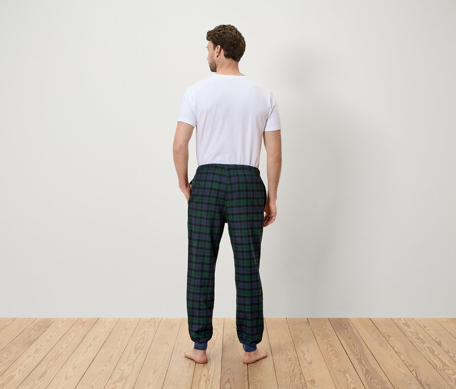 Un homme vu de dos porte un t-shirt blanc et un pantalon de pyjama à carreaux verts.