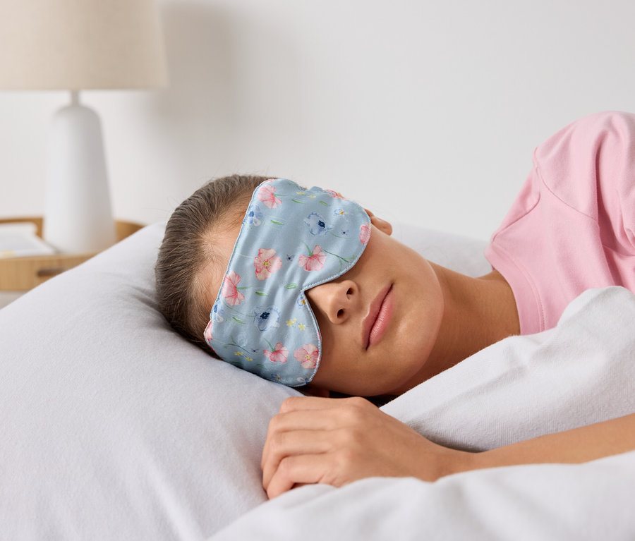 Une femme dort dans un lit avec un masque de sommeil à fleurs.