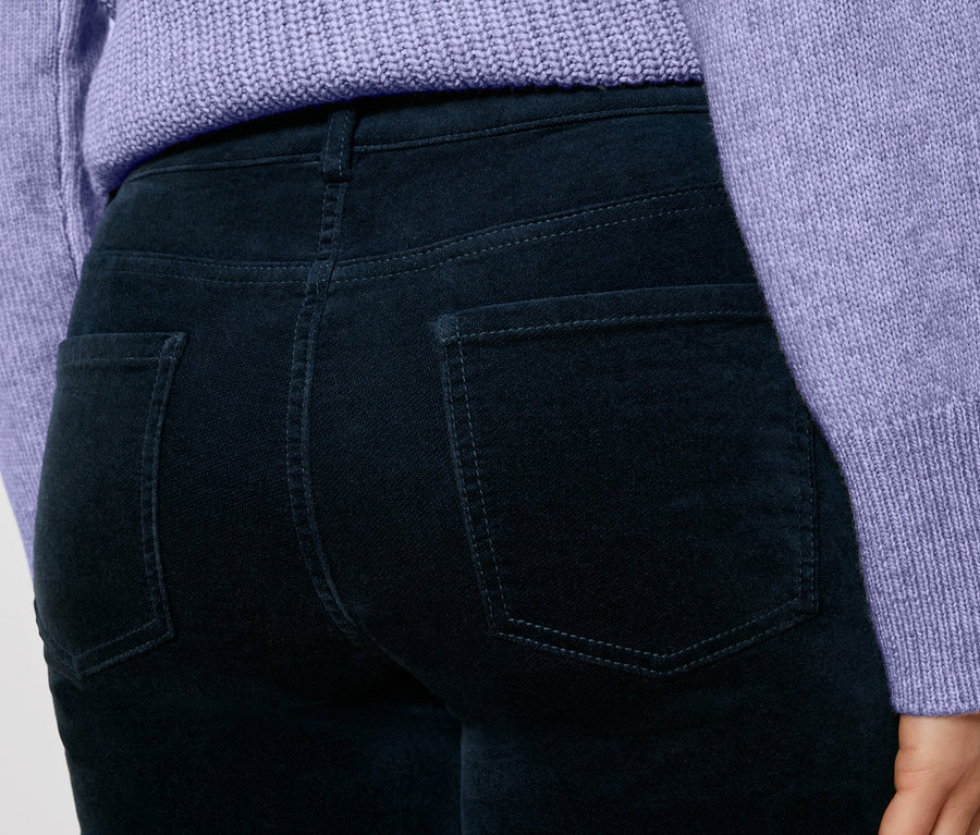 Gros plan sur une femme portant un pantalon en velours côtelé bleu foncé et un pull violet.