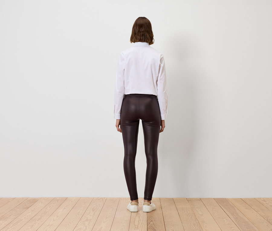 Femme vue de dos portant une chemise blanche et des leggings marron brillants.
