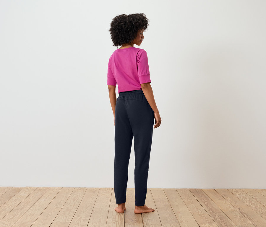 Vue arrière d'une femme avec un afro portant un t-shirt rose et un pantalon bleu marine.