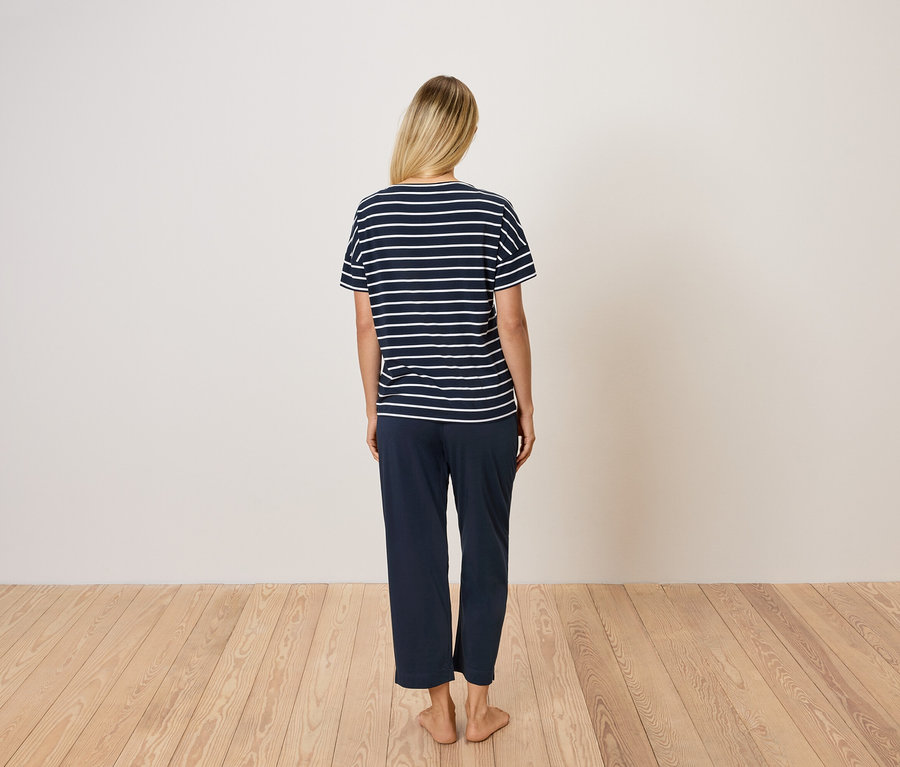 Vue de dos d'une femme blonde portant un t-shirt rayé bleu et un pantalon bleu.