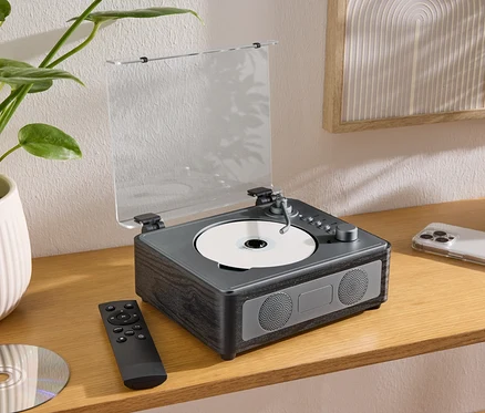 Sur une table se trouve un haut-parleur CD/Bluetooth® avec un CD, une télécommande et un téléphone portable.