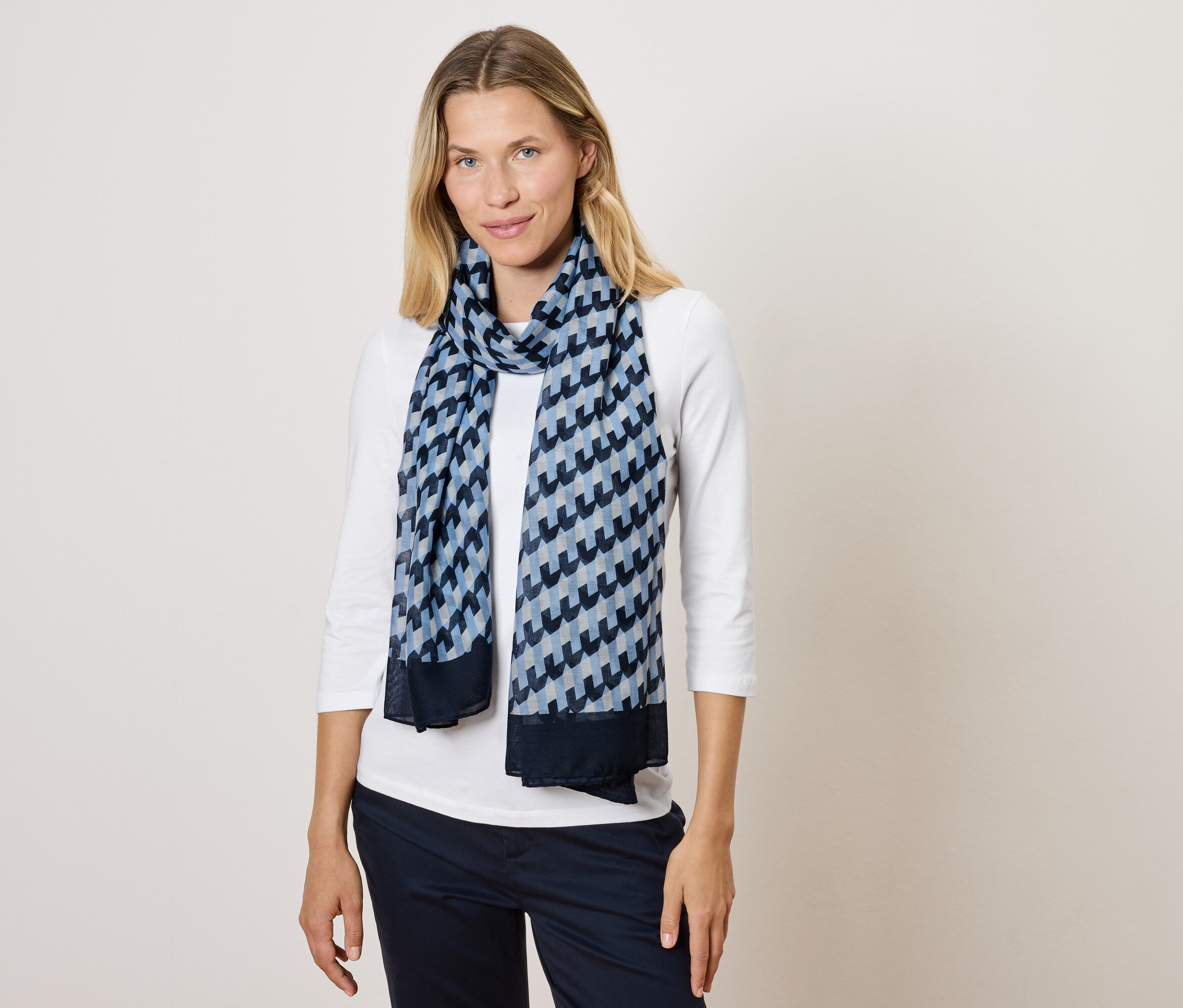 Femme blonde portant un foulard bleu et blanc et un t-shirt blanc.