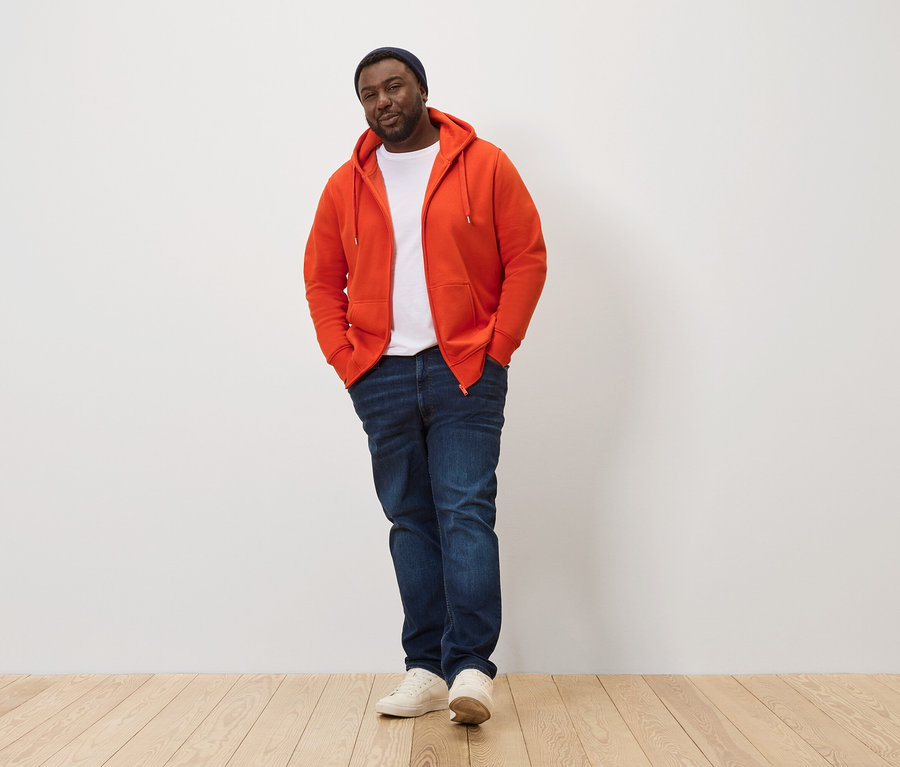 Un homme pose, portant une veste à capuche orange.