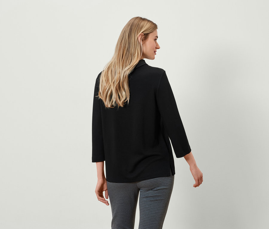 Vue de dos, femme blonde portant un haut noir à manches trois-quarts et un pantalon à carreaux gris.