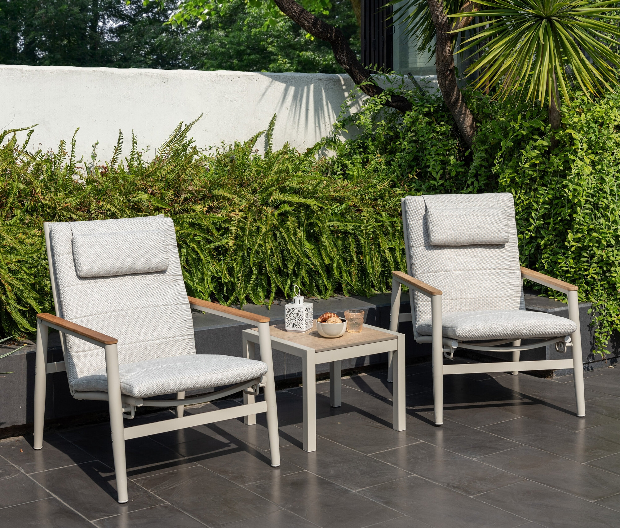 Deux fauteuils de salon d'extérieur ScanCom gris clair avec dossier réglable et une table avec des rafraîchissements sur une terrasse.