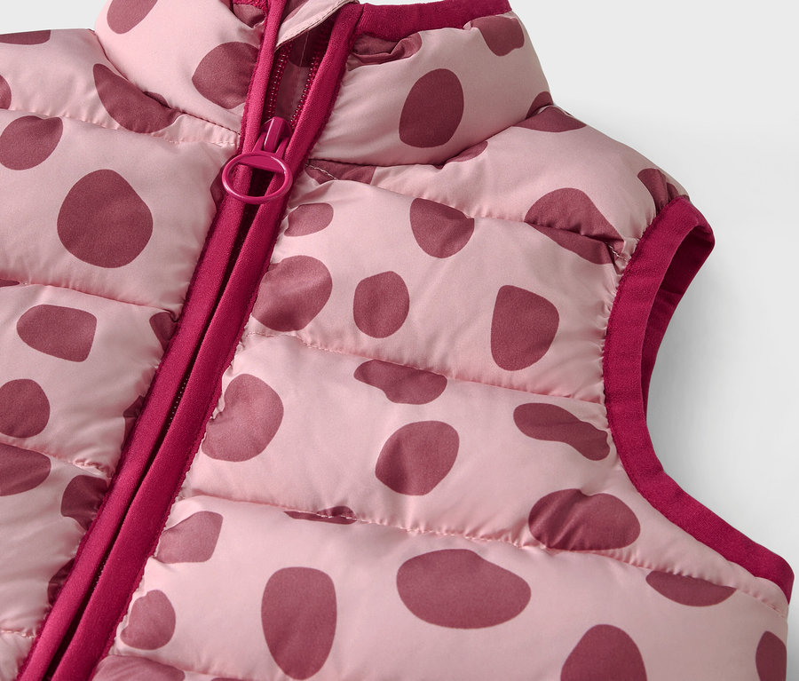 Détail d'un gilet matelassé rose avec des pois bordeaux et une fermeture éclair.