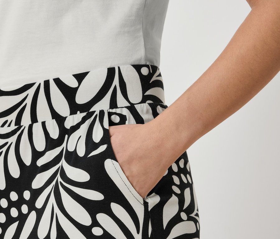 Gros plan d'une personne portant un pantalon avec un motif de feuilles noir et blanc et une main dans sa poche.