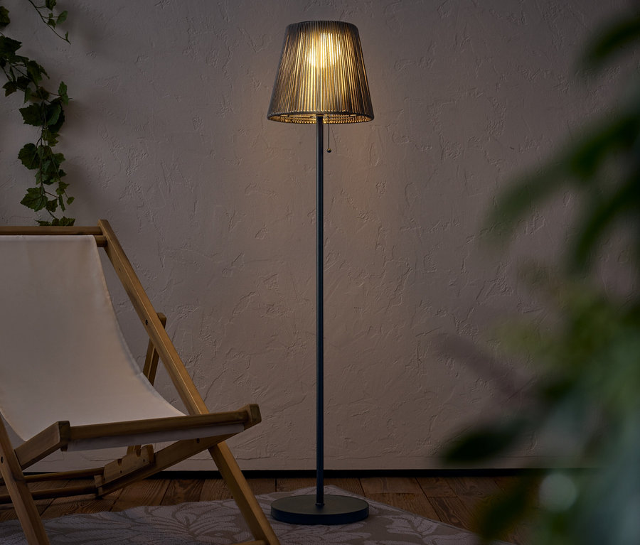 Un lampadaire éclairé avec un abat-jour se dresse à côté d'une chaise longue en bois.