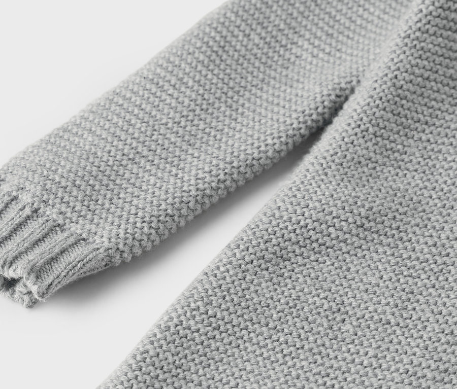 Vue détaillée d'un pull en tricot gris avec une manche et un poignet.