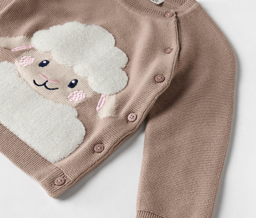 Gros plan sur un cardigan en tricot rose avec un mouton cousu.