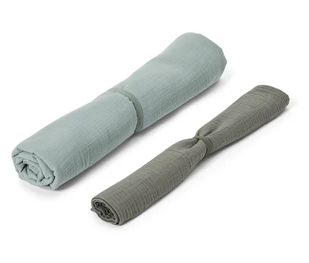 Deux langes en mousseline enroulés en bleu et gris reposent sur un fond blanc.