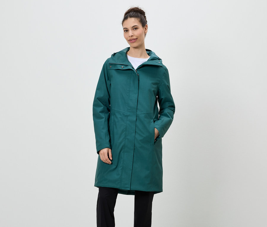 Femme debout portant un imperméable vert émeraude à capuche et un pantalon noir.