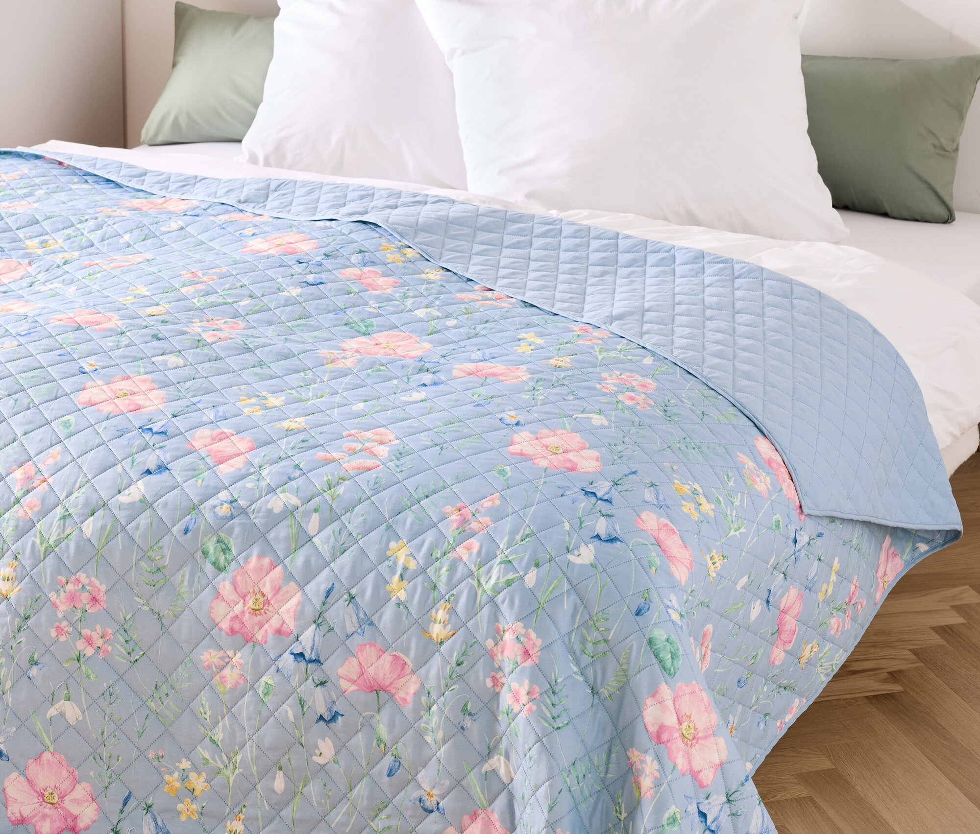 Jeté de lit bleu à motif floral sur un lit avec des coussins blancs.