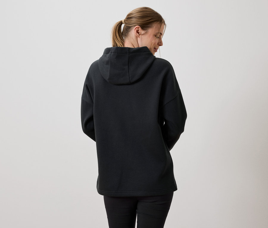 Vue arrière d'une femme aux cheveux blonds portant un sweat à capuche noir et un legging noir.