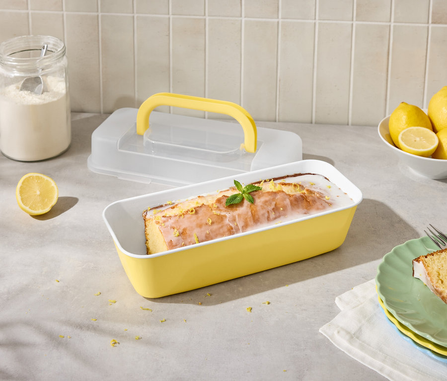 Gâteau au citron dans un moule jaune avec des citrons et un glaçage, coupé en tranches dans une assiette avec une fourchette.