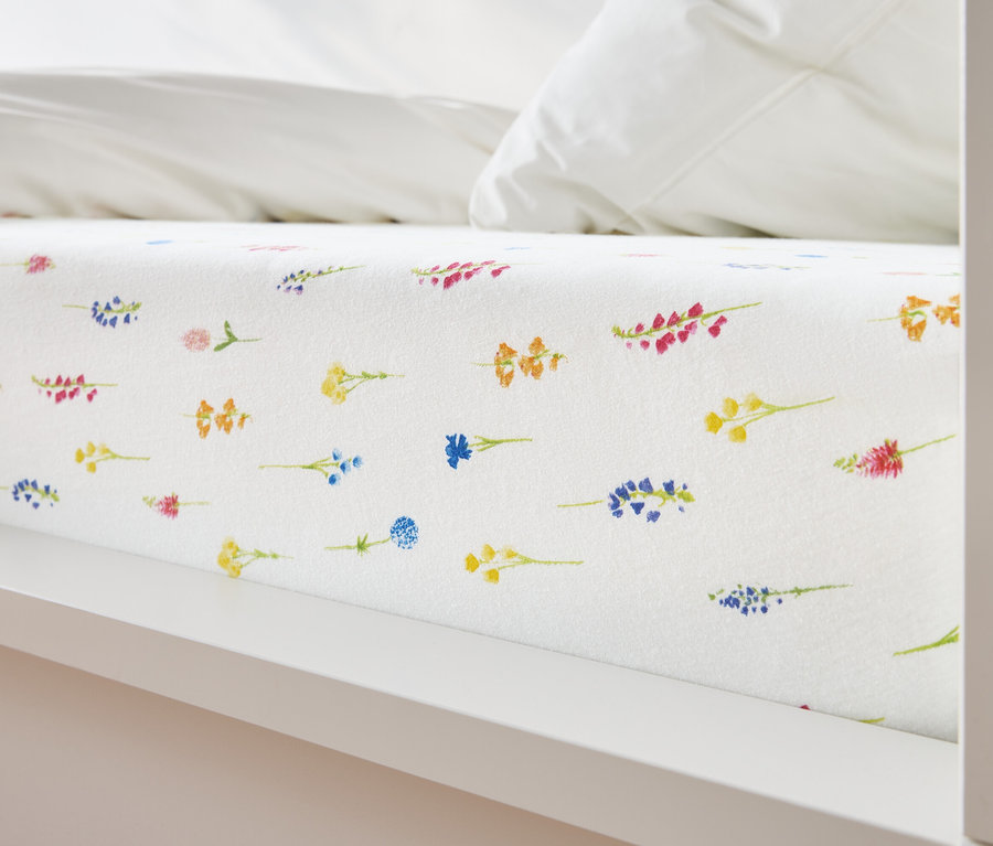 Gros plan d'un lit avec un drap blanc recouvert d'un motif floral jaune, bleu, orange et rose.