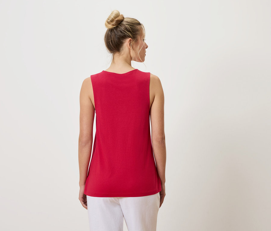 Vue de dos d'une femme avec un chignon portant un débardeur rouge et un pantalon blanc.