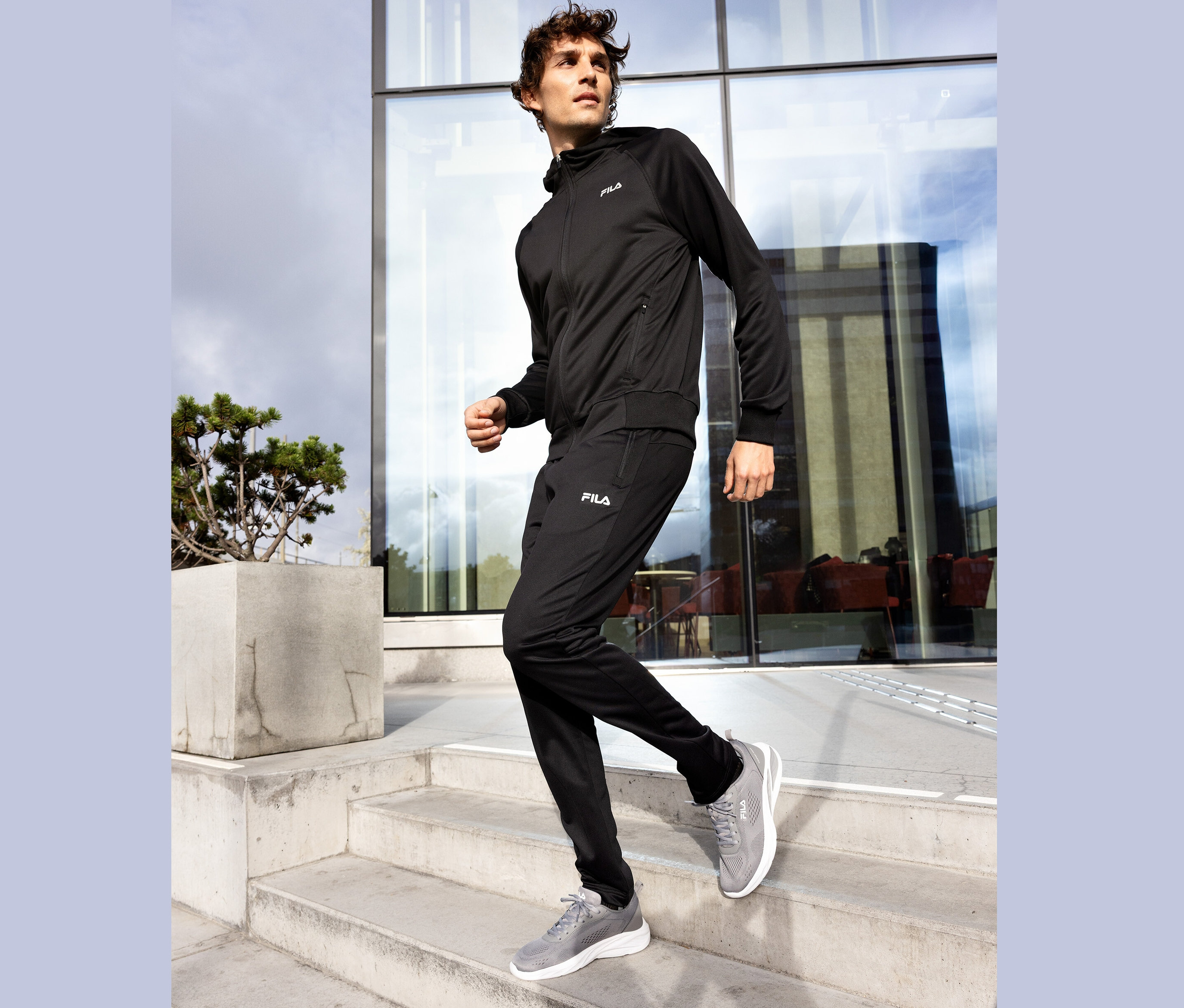 Homme en survêtement Fila noir et baskets grises descendant un escalier en béton.
