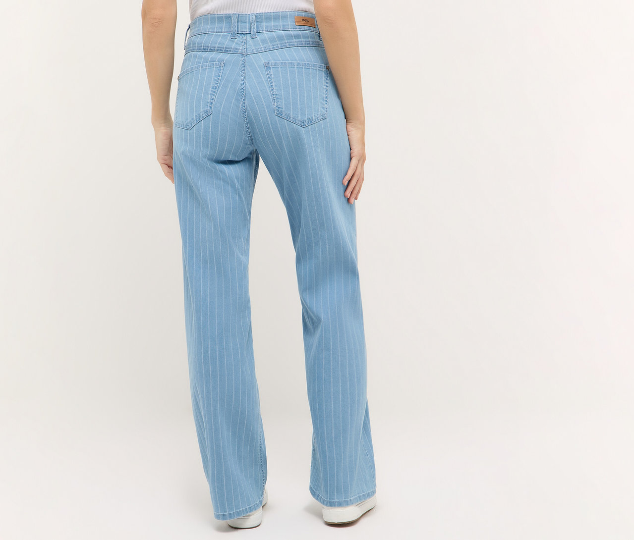 Vue arrière d'une femme portant un jean Angels Denim «
Liz » Wide Leg à rayures claires et des chaussures blanches sur un fond clair.