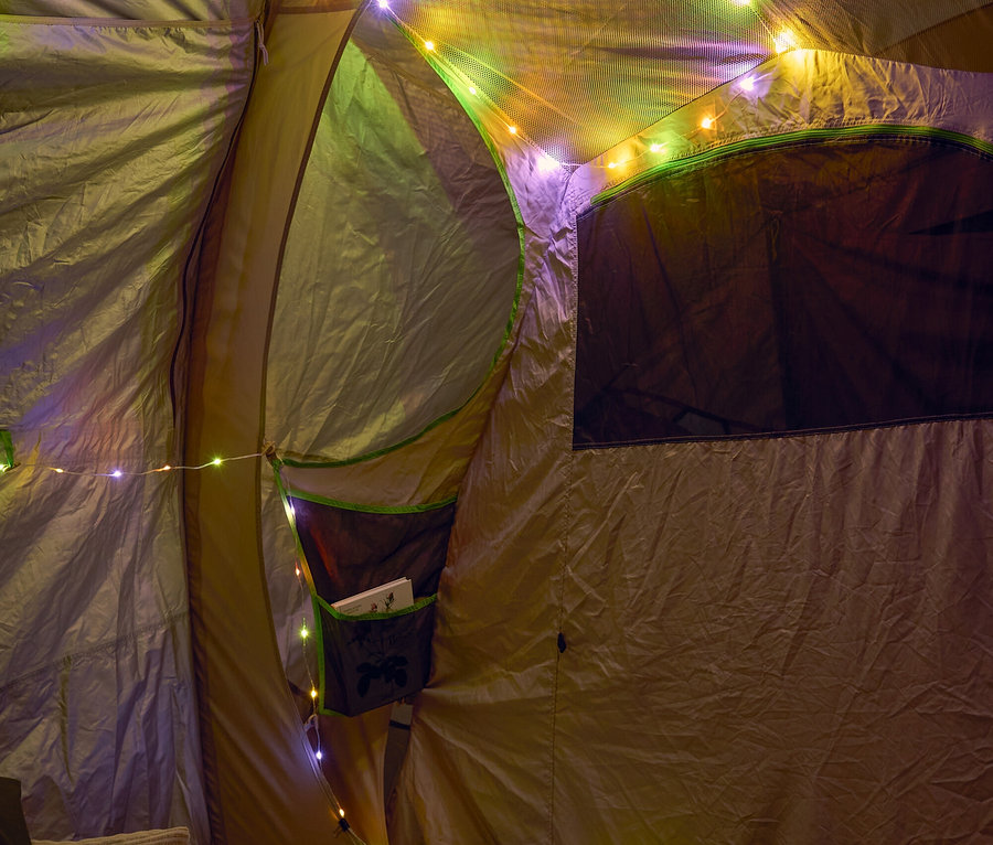 Intérieur d'une tente décorée de lumières colorées, avec des coussins et un pouf au premier plan.