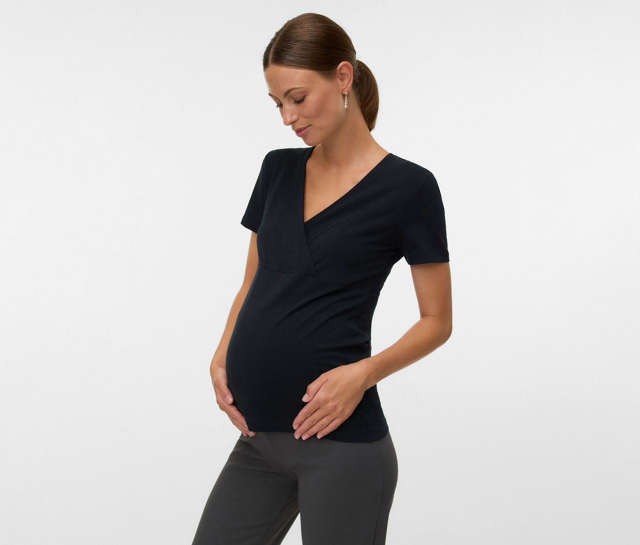 Femme enceinte portant un lot de 2 t-shirts MAMALICIOUS «
MLKERRIE TESS » noir et un pantalon gris, les mains sur le ventre.