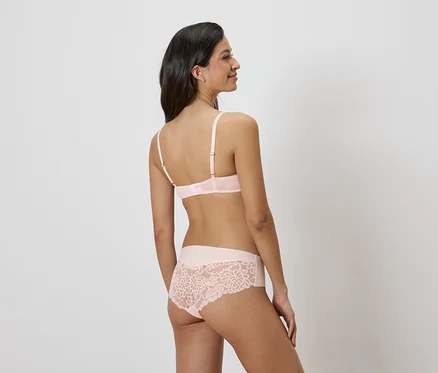 Vue arrière d'une femme aux longs cheveux foncés portant un soutien-gorge rose clair et des sous-vêtements assortis avec des détails en dentelle.
