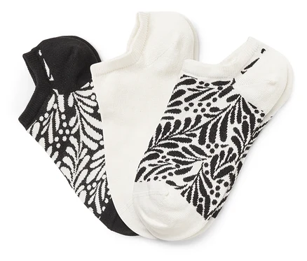 Trois chaussettes sont côte à côte : une noire avec un motif de feuilles blanches, une blanche et une blanche avec un motif de feuilles noires.