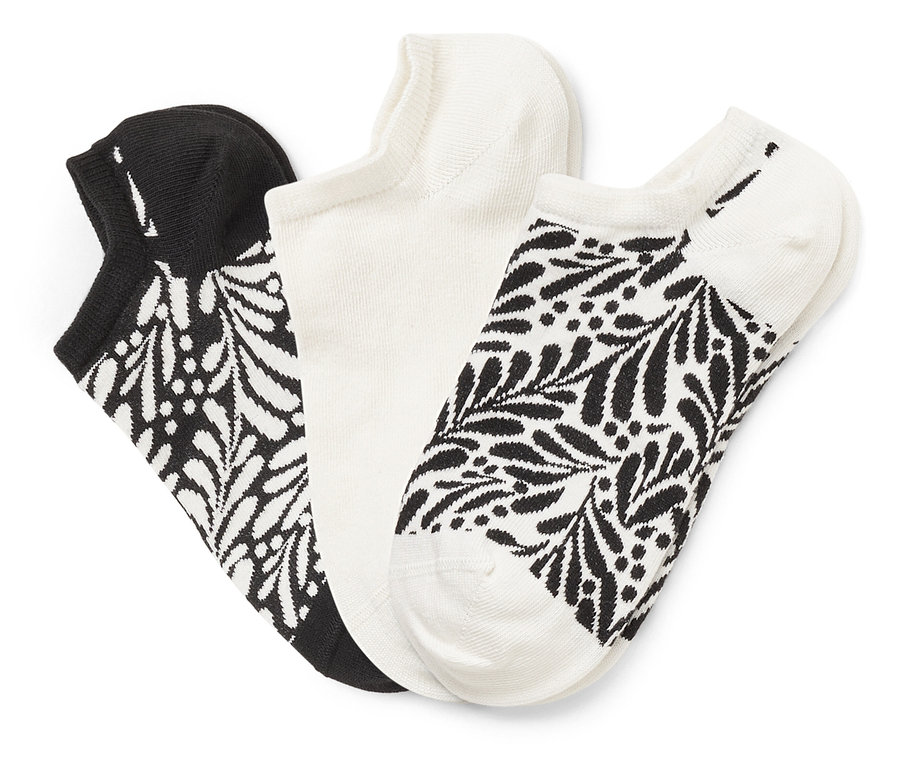 Trois chaussettes sont côte à côte : une noire avec un motif de feuilles blanches, une blanche et une blanche avec un motif de feuilles noires.