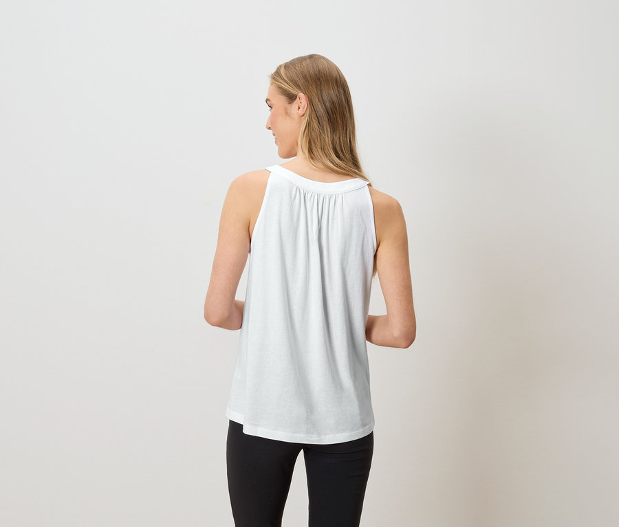 Femme vue de dos portant un débardeur blanc et un pantalon noir.