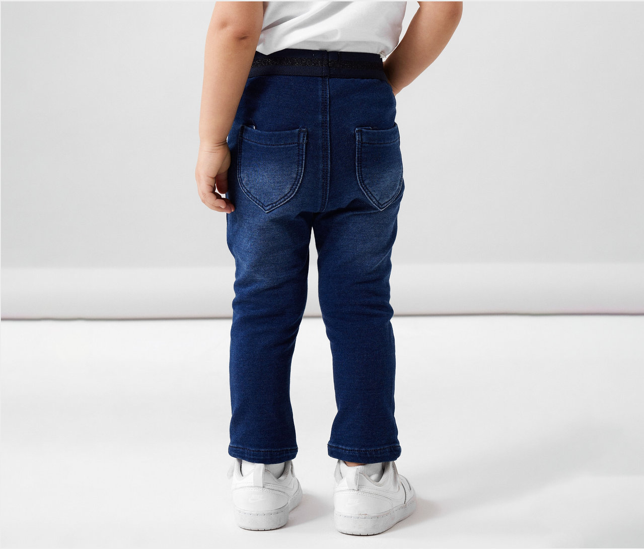 Vue arrière d'un enfant portant un jean en sweat NAME IT et des baskets blanches.
