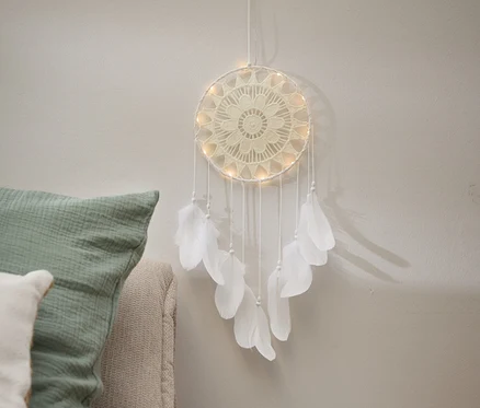 Un attrape-rêves crème avec des plumes est accroché à un mur à côté d'une table de chevet.
