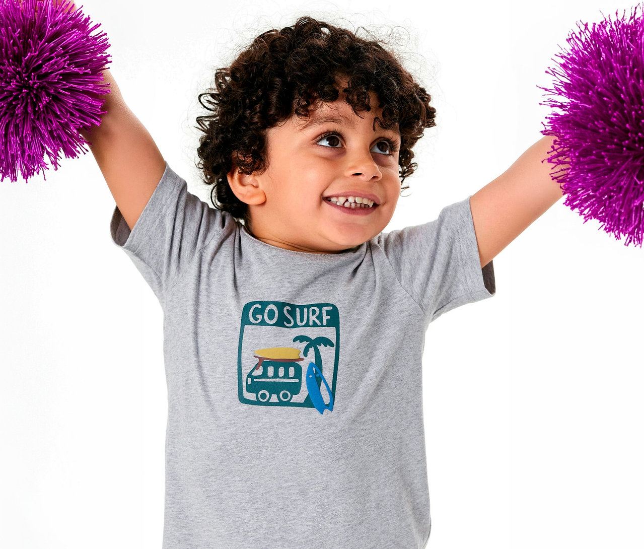 Garçon aux cheveux bouclés portant un haut de pyjama court pour enfant SCHIESSER tenant des pompons violets.