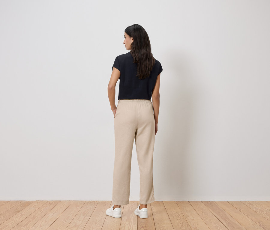 Vue de dos d'une femme aux cheveux foncés portant un t-shirt noir, un pantalon beige et des baskets blanches.
