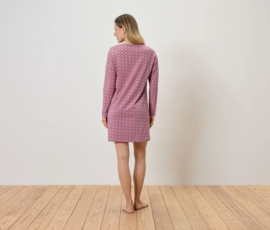 Une femme blonde se tient dos au spectateur et porte une robe courte rose à motifs avec des manches longues.