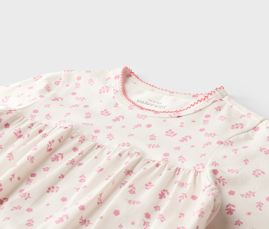Gros plan sur une robe blanche pour enfant avec un motif floral rose et un ourlet rose à l'encolure.