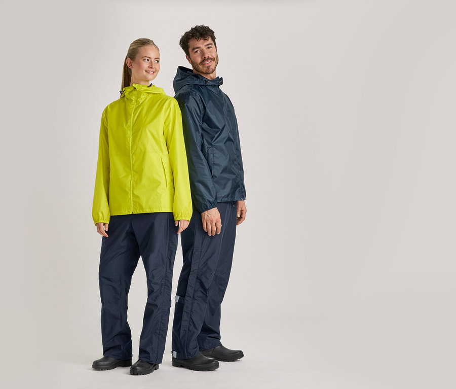 Une femme portant une veste de pluie jaune et un homme portant une veste de pluie bleu marine et un pantalon de pluie se tiennent devant un fond gris.