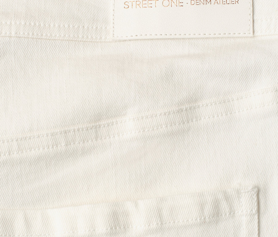 Gros plan sur un Jeans Street One blanc avec une étiquette claire affichant le texte 'designed with passion STREET ONE - DENIM ATELIER'.