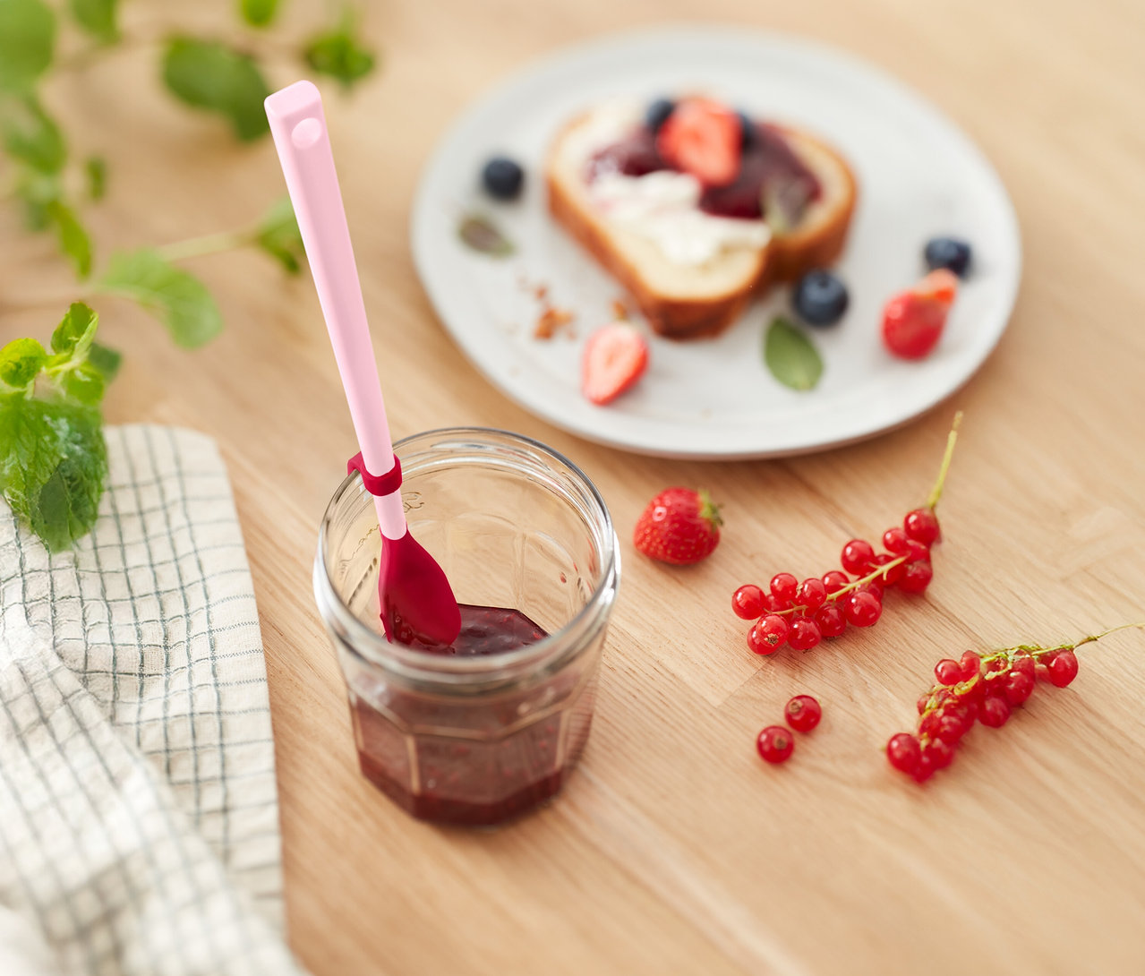 Pot de confiture avec une cuillère rose, pain grillé aux fraises et aux myrtilles et groseilles sur une table en bois.