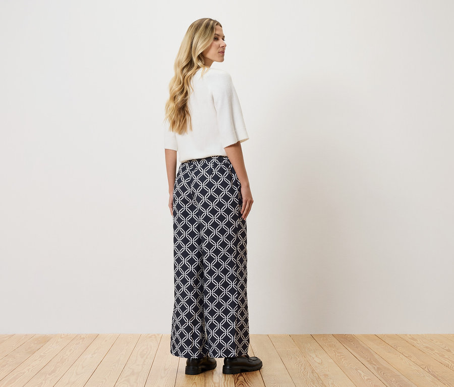 Femme portant un haut blanc et un pantalon long bleu marine avec un motif géométrique blanc.