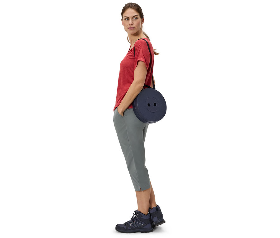 Femme portant un t-shirt rouge et un pantalon gris, avec un tabouret rond bleu marine sur l'épaule.