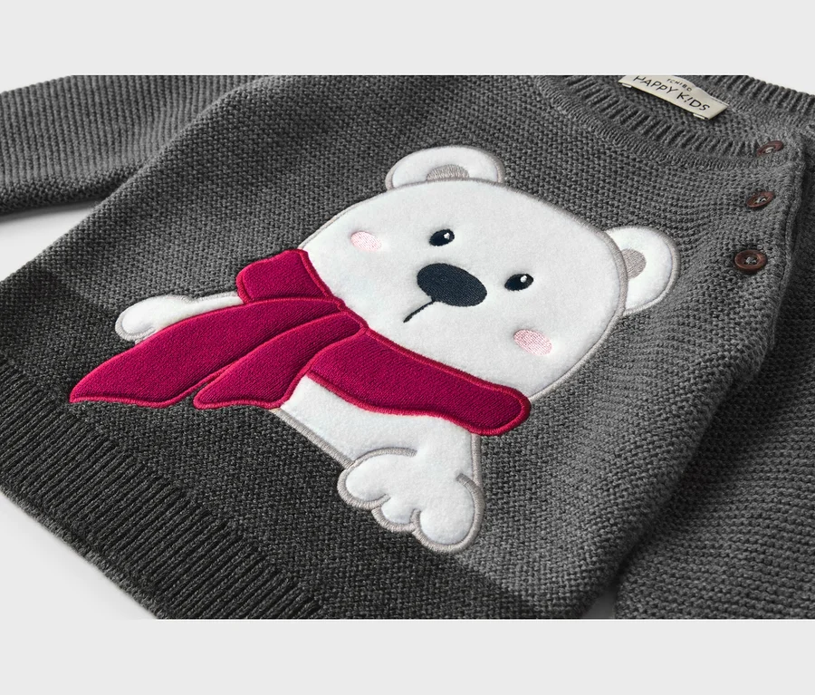 Pull en tricot gris avec une application d'ours polaire blanc portant une écharpe rouge et ayant des joues roses. Boutons marron sur l'épaule.