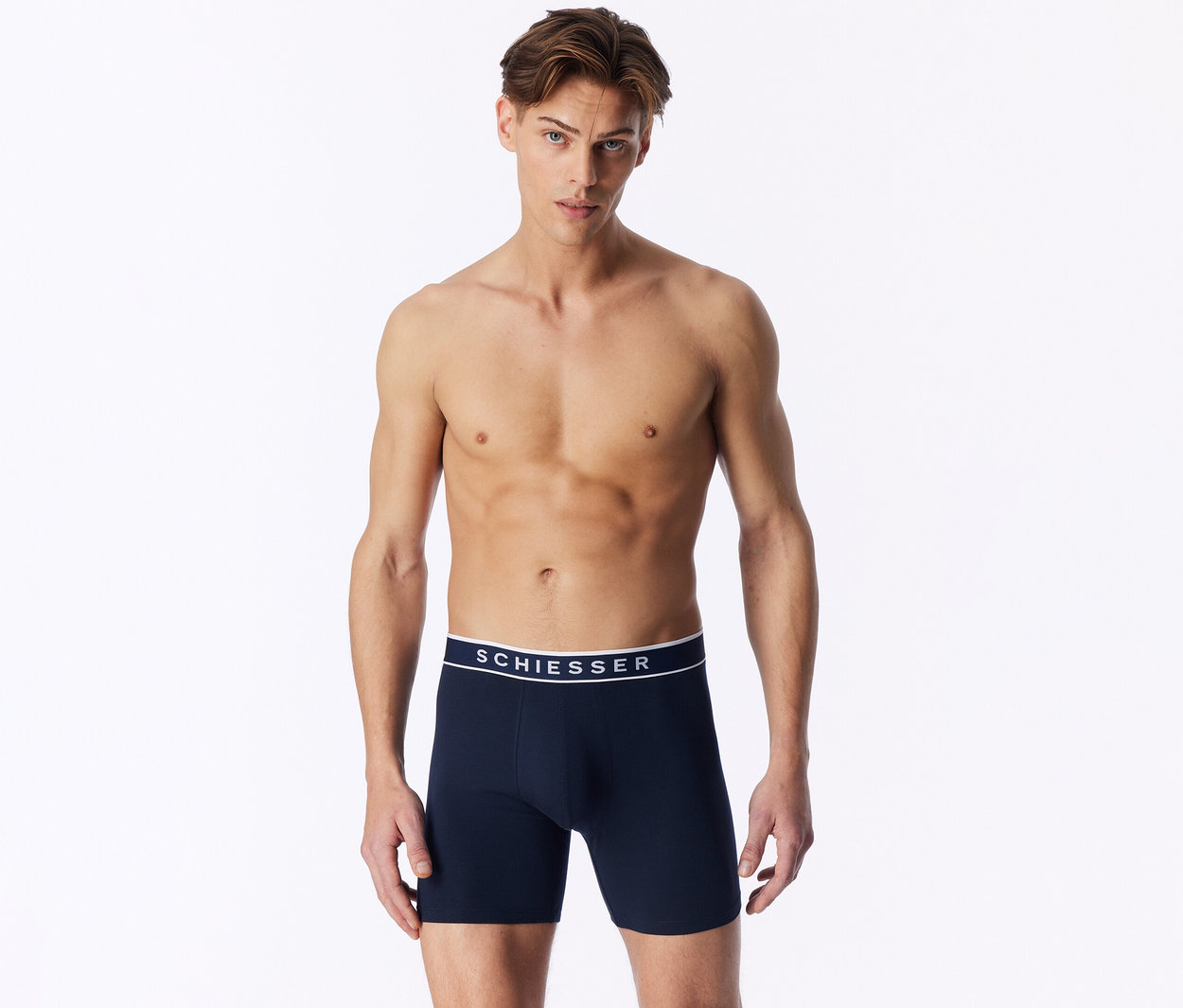 Un homme torse nu porte un boxer bleu foncé avec une ceinture blanche SCHIESSER.